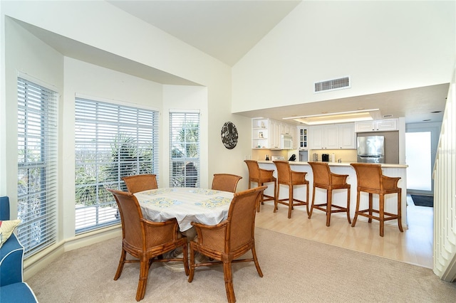 dining room featuring high vaulted ceiling and light carpet