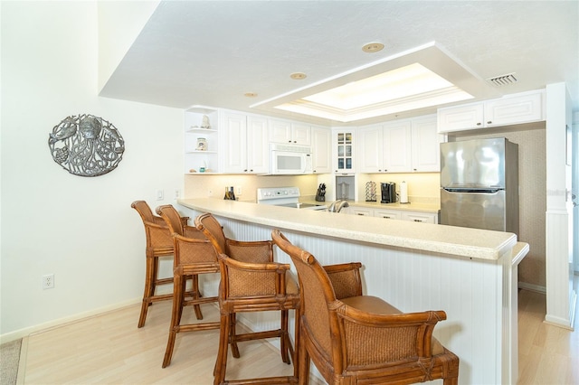 kitchen with white cabinetry, range, stainless steel refrigerator, kitchen peninsula, and a raised ceiling