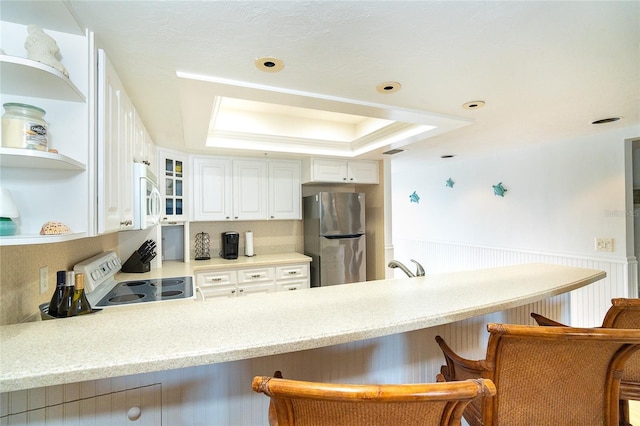 kitchen featuring a tray ceiling, white appliances, white cabinets, and a kitchen bar