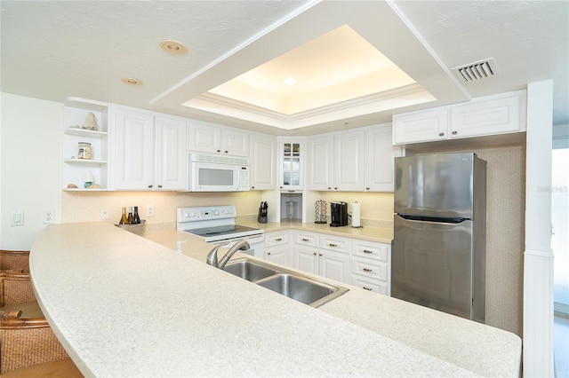 kitchen featuring sink, white appliances, white cabinetry, a tray ceiling, and kitchen peninsula