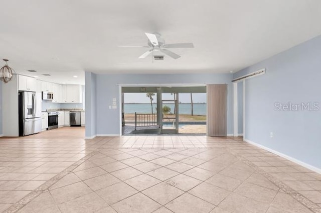 unfurnished living room featuring light tile patterned flooring, ceiling fan, and a water view