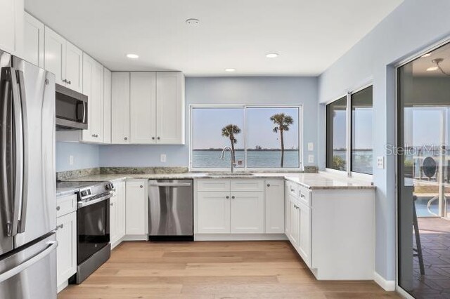 kitchen with sink, white cabinetry, light hardwood / wood-style flooring, appliances with stainless steel finishes, and light stone countertops