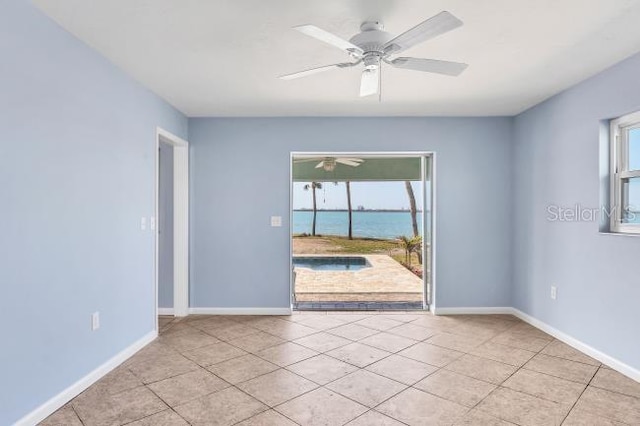 spare room featuring plenty of natural light, light tile patterned flooring, ceiling fan, and a water view