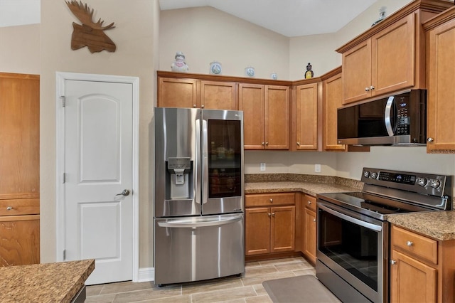 kitchen with lofted ceiling, light stone countertops, and appliances with stainless steel finishes