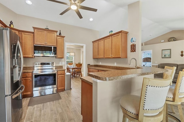 kitchen featuring lofted ceiling, light hardwood / wood-style flooring, appliances with stainless steel finishes, a kitchen breakfast bar, and kitchen peninsula