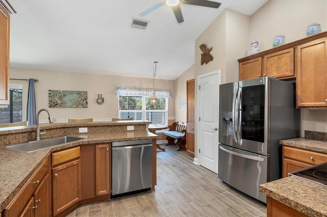 kitchen featuring pendant lighting, sink, lofted ceiling, appliances with stainless steel finishes, and light wood-type flooring