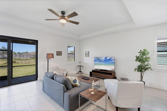 tiled living room with a raised ceiling and ceiling fan