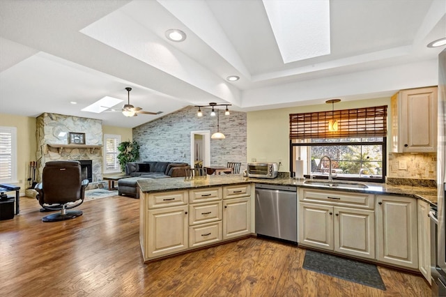 kitchen featuring stainless steel dishwasher, a sink, a peninsula, a fireplace, and vaulted ceiling with skylight