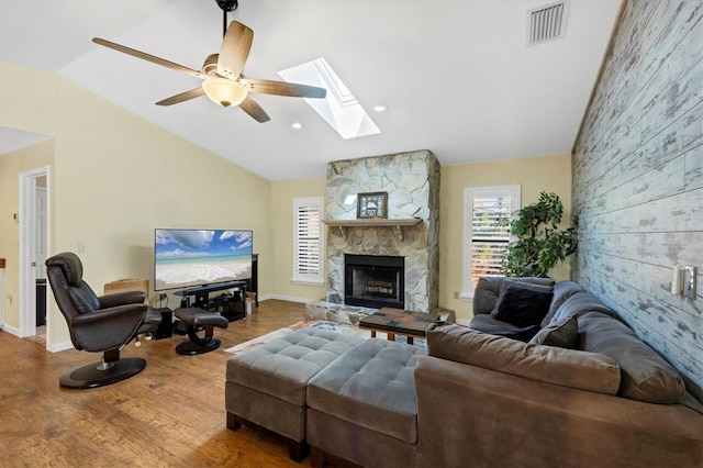 living room featuring wood finished floors, vaulted ceiling with skylight, visible vents, a stone fireplace, and an accent wall