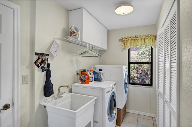 clothes washing area featuring a sink, cabinet space, washing machine and clothes dryer, light tile patterned floors, and baseboards