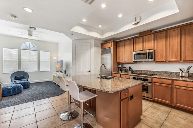 kitchen featuring sink, light tile patterned floors, a raised ceiling, an island with sink, and stainless steel appliances