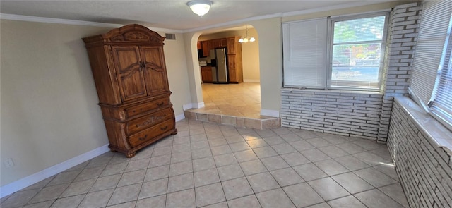 spare room with crown molding, brick wall, and light tile patterned floors