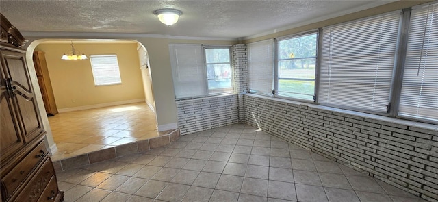 tiled empty room featuring crown molding, brick wall, a textured ceiling, and a wealth of natural light