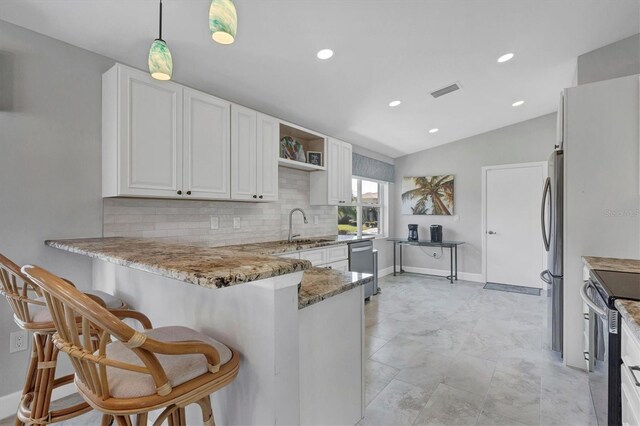 kitchen featuring lofted ceiling, appliances with stainless steel finishes, a sink, light stone countertops, and a peninsula