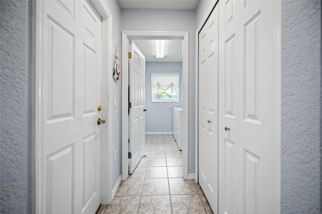 hallway with separate washer and dryer and light tile patterned flooring