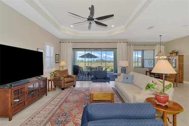 tiled living room featuring crown molding, ceiling fan with notable chandelier, and a raised ceiling