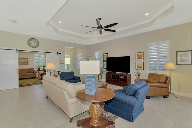 tiled living room featuring ornamental molding, a barn door, ceiling fan, and a tray ceiling