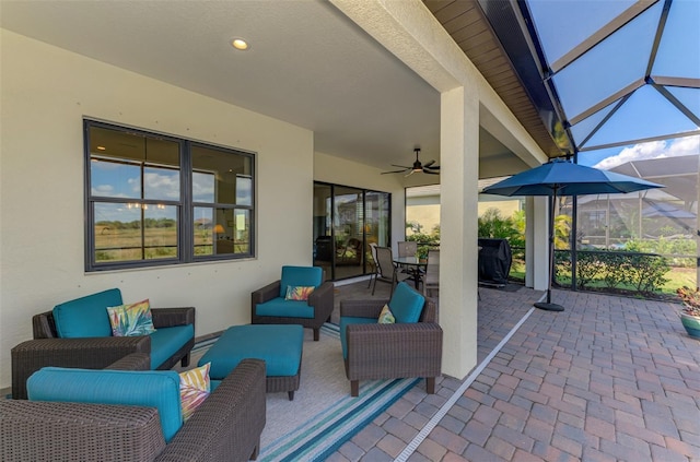 view of patio featuring ceiling fan, an outdoor living space, and glass enclosure