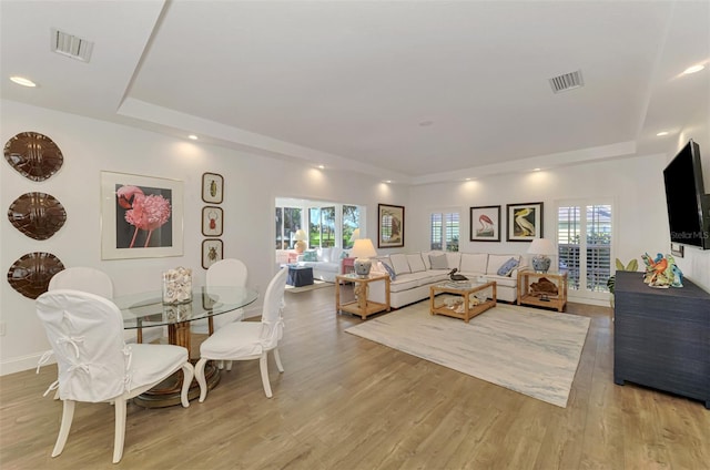 living room featuring a wealth of natural light, light wood-type flooring, and a tray ceiling