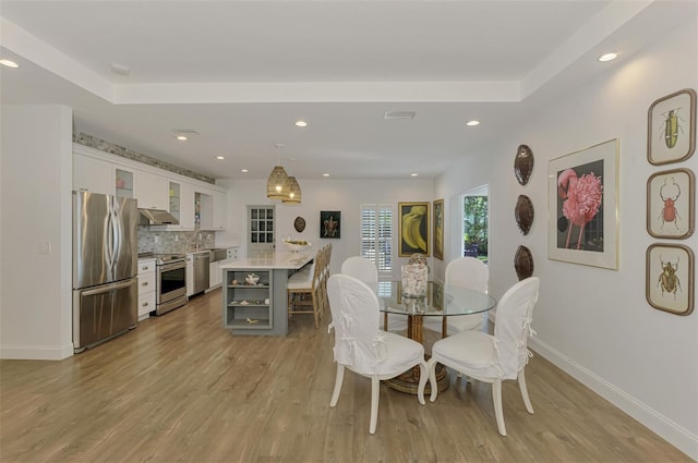 dining space featuring sink, a raised ceiling, and light hardwood / wood-style floors