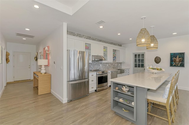 kitchen with appliances with stainless steel finishes, pendant lighting, a breakfast bar area, white cabinets, and light hardwood / wood-style floors