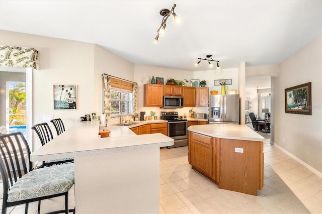 kitchen with a breakfast bar, sink, light tile patterned floors, kitchen peninsula, and stainless steel appliances