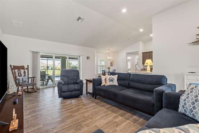 living room featuring lofted ceiling, a chandelier, and light hardwood / wood-style floors