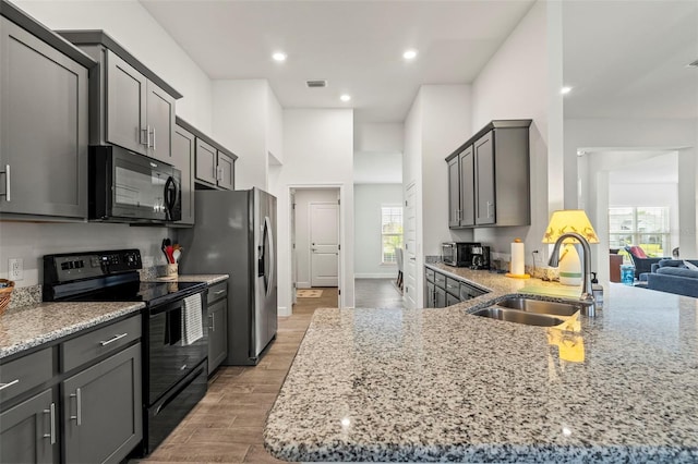 kitchen with sink, light stone counters, light hardwood / wood-style flooring, a kitchen island, and black appliances