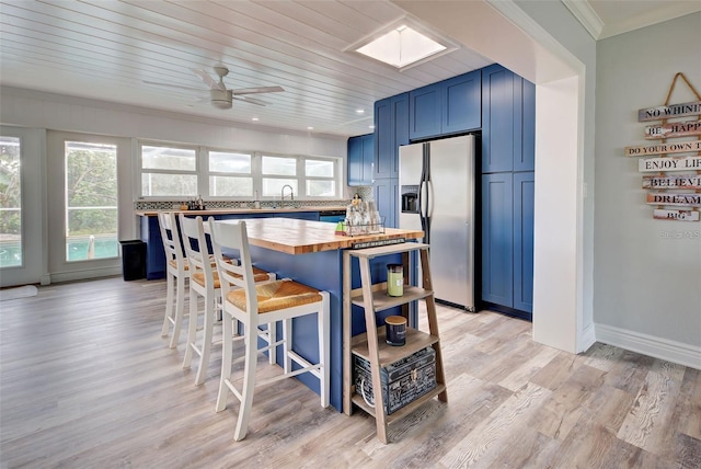 kitchen with stainless steel refrigerator with ice dispenser, a healthy amount of sunlight, wooden counters, and blue cabinetry