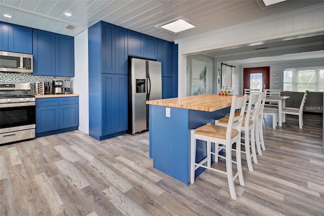 kitchen featuring butcher block countertops, a breakfast bar area, blue cabinetry, and appliances with stainless steel finishes