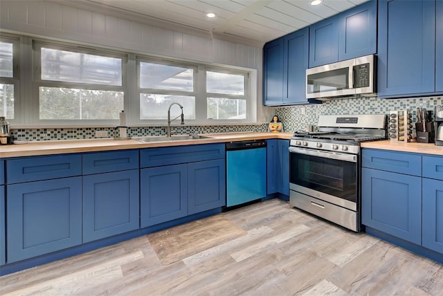 kitchen with sink, appliances with stainless steel finishes, butcher block counters, blue cabinets, and decorative backsplash