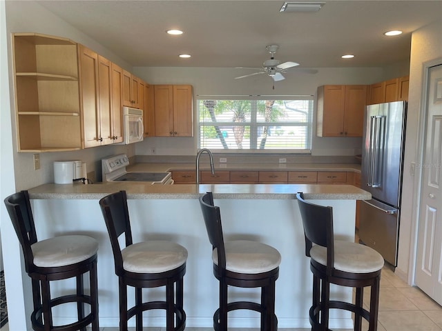 kitchen with white appliances, a kitchen breakfast bar, light tile patterned flooring, light brown cabinetry, and kitchen peninsula