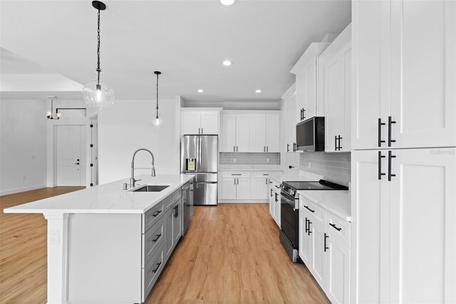 kitchen featuring white cabinets, a kitchen island with sink, stainless steel appliances, pendant lighting, and a sink