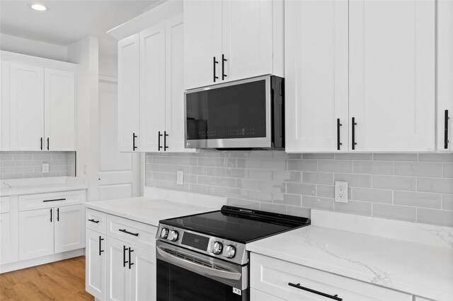 kitchen with light stone counters, stainless steel appliances, white cabinetry, light wood-style floors, and tasteful backsplash