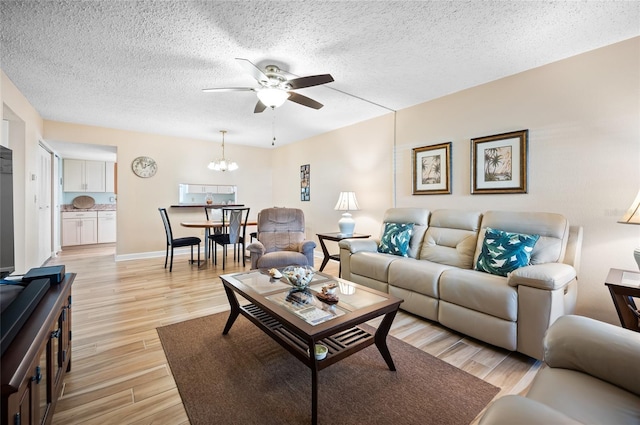 living room featuring ceiling fan with notable chandelier, light hardwood / wood-style floors, and a textured ceiling