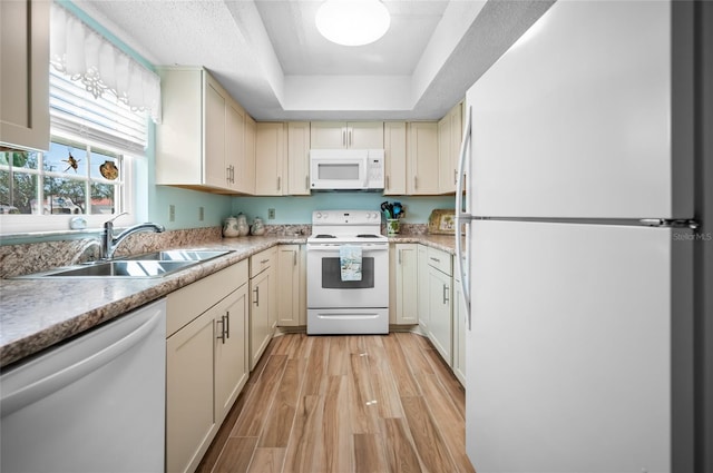 kitchen featuring sink, white appliances, cream cabinets, a tray ceiling, and light hardwood / wood-style floors