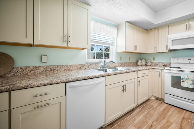 kitchen with sink, a textured ceiling, white appliances, light hardwood / wood-style floors, and cream cabinetry