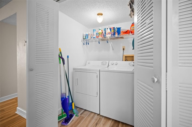 clothes washing area featuring washing machine and clothes dryer, a textured ceiling, and light wood-type flooring