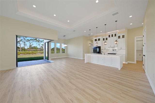 unfurnished living room with a towering ceiling, a raised ceiling, and light wood-type flooring