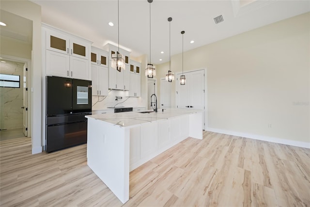 kitchen featuring black refrigerator, pendant lighting, white cabinetry, light stone counters, and a spacious island