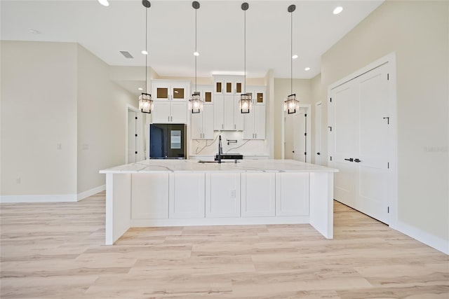 kitchen featuring white cabinetry, sink, hanging light fixtures, light stone counters, and a spacious island