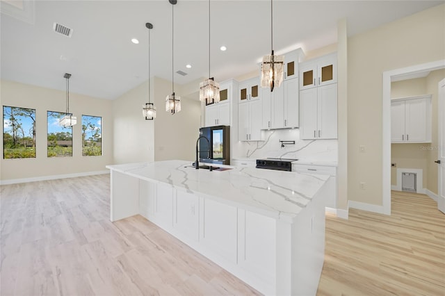 kitchen with pendant lighting, white cabinetry, backsplash, a large island with sink, and light stone counters