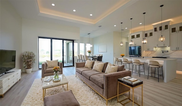 living room featuring a towering ceiling, light wood-type flooring, and a tray ceiling