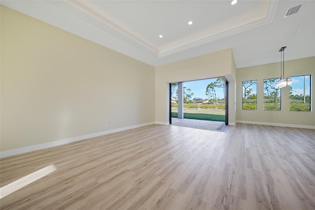 spare room with crown molding, a towering ceiling, light wood-type flooring, and a tray ceiling