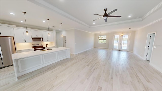 unfurnished living room with pendant lighting, a center island with sink, white cabinets, and a tray ceiling