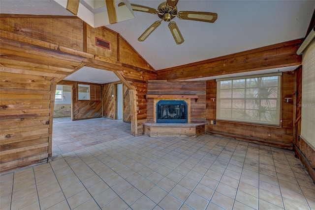 unfurnished living room featuring light tile patterned floors, visible vents, a glass covered fireplace, ceiling fan, and wooden walls