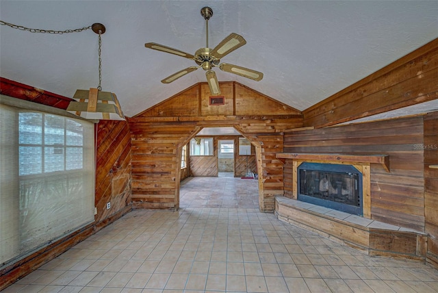 unfurnished living room with lofted ceiling, wood walls, a fireplace, a ceiling fan, and tile patterned floors