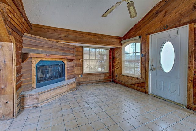 entryway featuring light tile patterned floors, a fireplace with raised hearth, ceiling fan, vaulted ceiling, and wooden walls