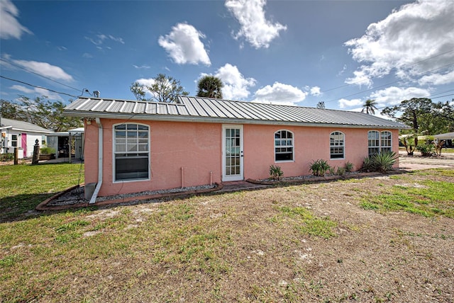 back of house featuring metal roof, a lawn, and stucco siding