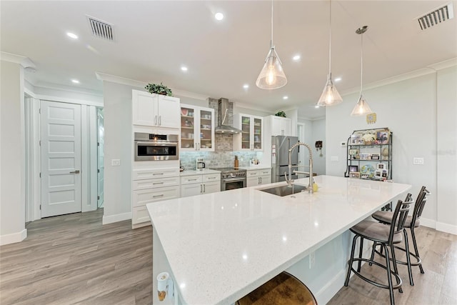 kitchen with appliances with stainless steel finishes, a kitchen breakfast bar, decorative light fixtures, wall chimney exhaust hood, and a spacious island